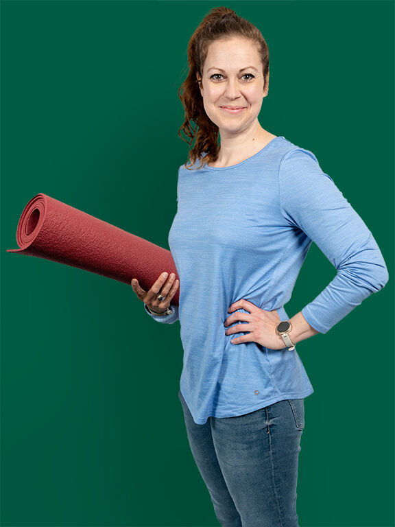 Julia Siart-Amstätter lächelt mit einer Yogamatte in der Hand in die Kamera