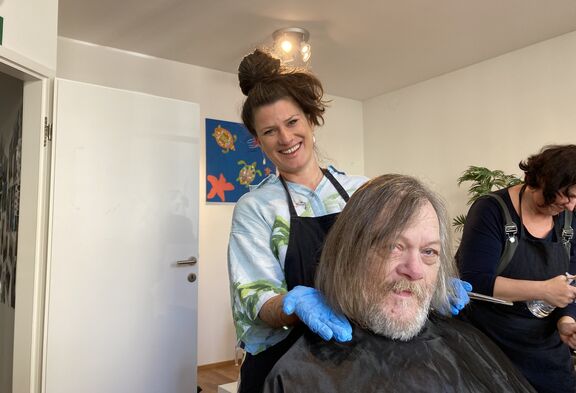 Eine Friseurin steht hinter einem Mann mit frisch geschnittenen Haaren und lacht.