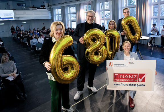 FSW Geschäftsführerin Anita Bauer, Stadtrat Peter Hacker, Gabriele Zgubic (AK Wien), Bildungsdirektor Heinrich Himmer und die Leiterin der FSW Finanzbildung Gudrun Steinmann halten auf der Bühne die Zahl 6.800 in Form von goldenen Luftballons und eine Tafel mit dem Logo des Finanzführerscheins in die Kamera.